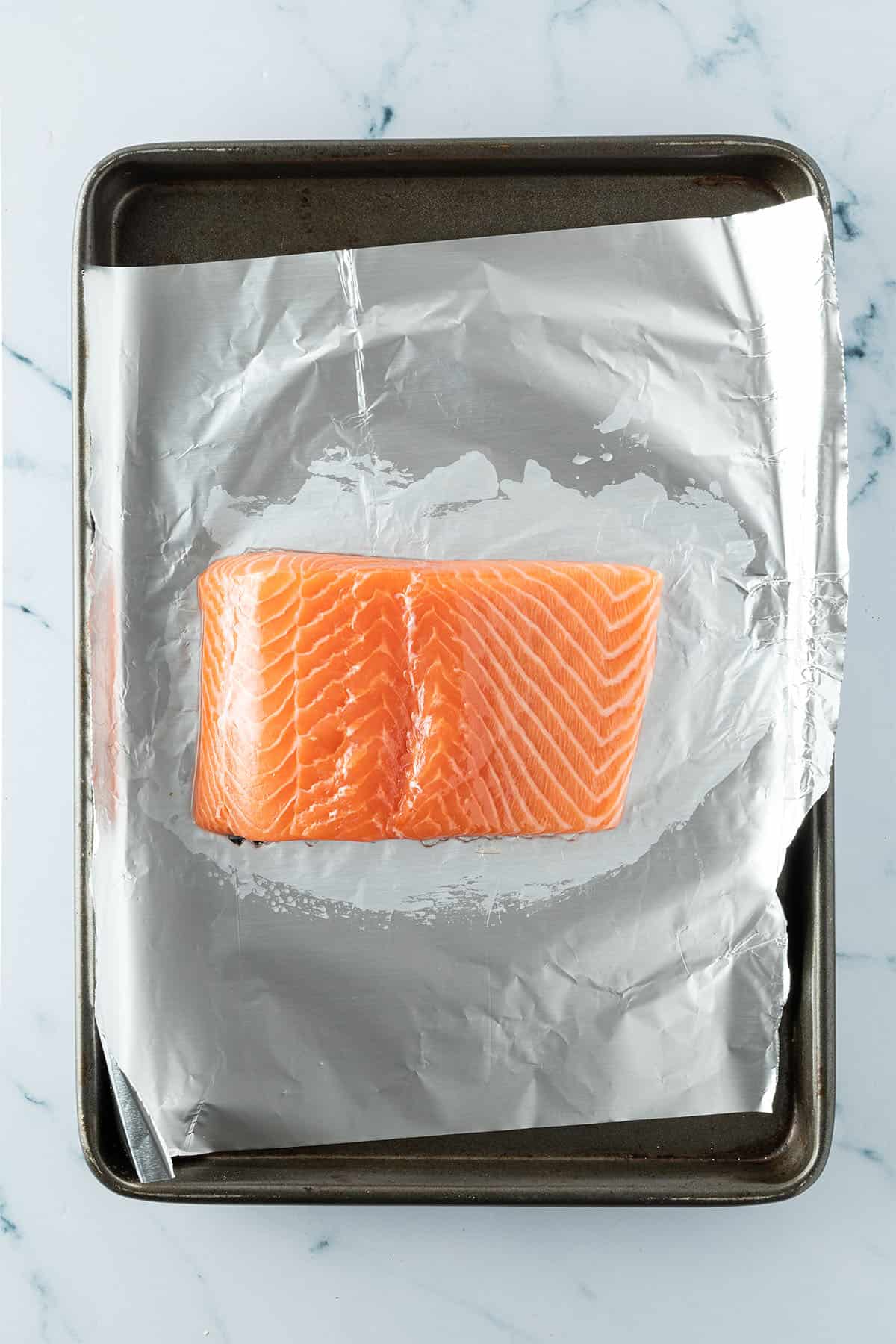 Ein rohes Lachsfilet auf einem Blech mit Aluminiumfolie.