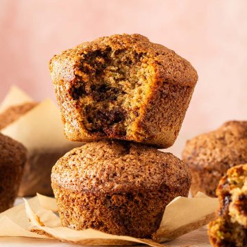 Zucchini Muffins mit saftiger Krume und geschmolzenen Schokost&uuml;ckchen, zwei davon aufeinander gestapelt, ein Muffin angebissen.