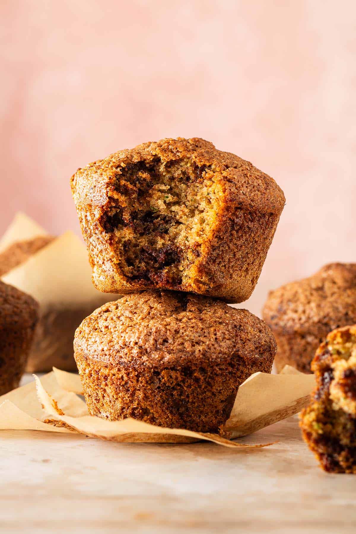 Zucchini Muffins mit saftiger Krume und geschmolzenen Schokost&uuml;ckchen, zwei davon aufeinander gestapelt, ein Muffin angebissen.