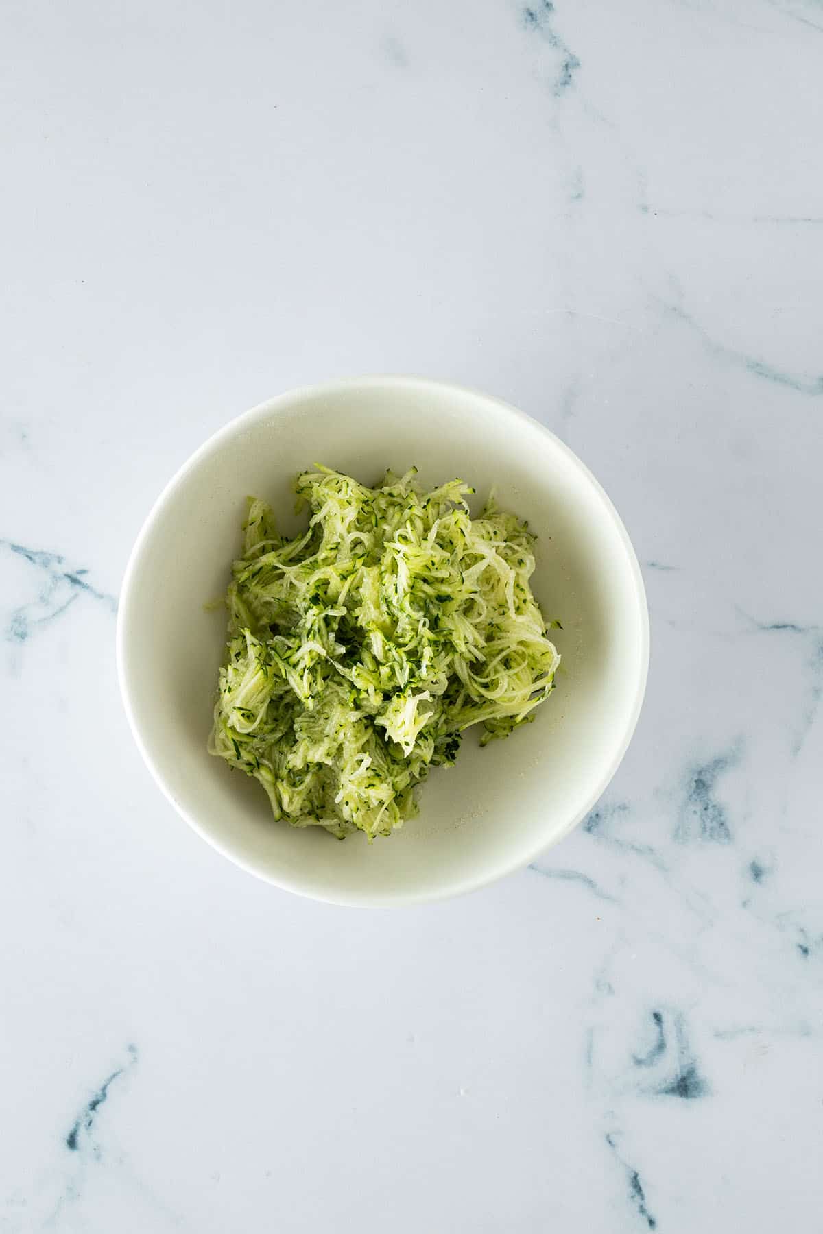 Fein geriebene Zucchini in einer Sch&uuml;ssel als Zutat f&uuml;r saftige Zucchini Muffins.