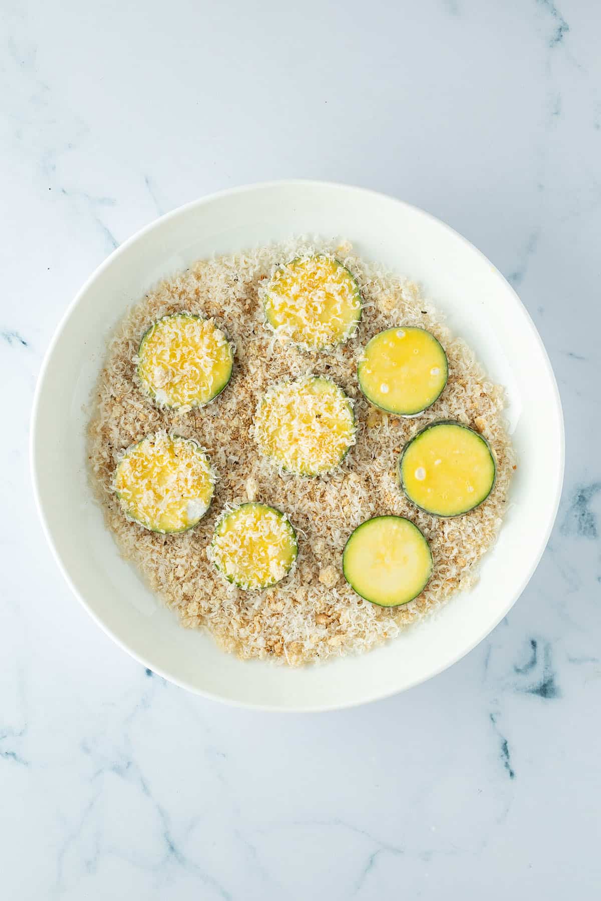 Zucchini Scheiben werden in einer Parmesan-Semmelbr&ouml;sel-Mischung paniert.