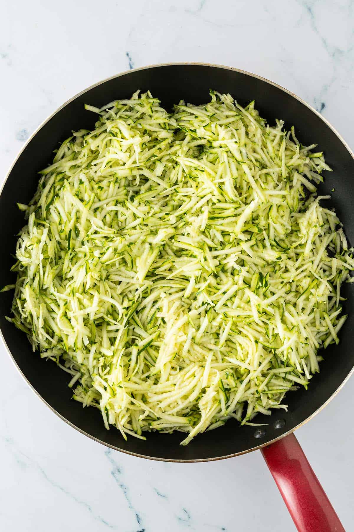 Grob geraspelte Zucchini in einer Pfanne als Basis f&uuml;r die Zucchini-Sauce.