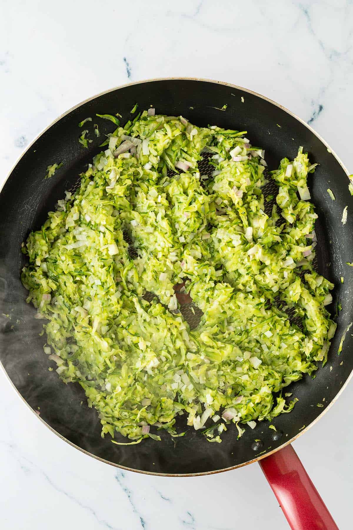 Geraspelte Zucchini und fein gew&uuml;rfelte Schalotten beim Anbraten in einer Pfanne.