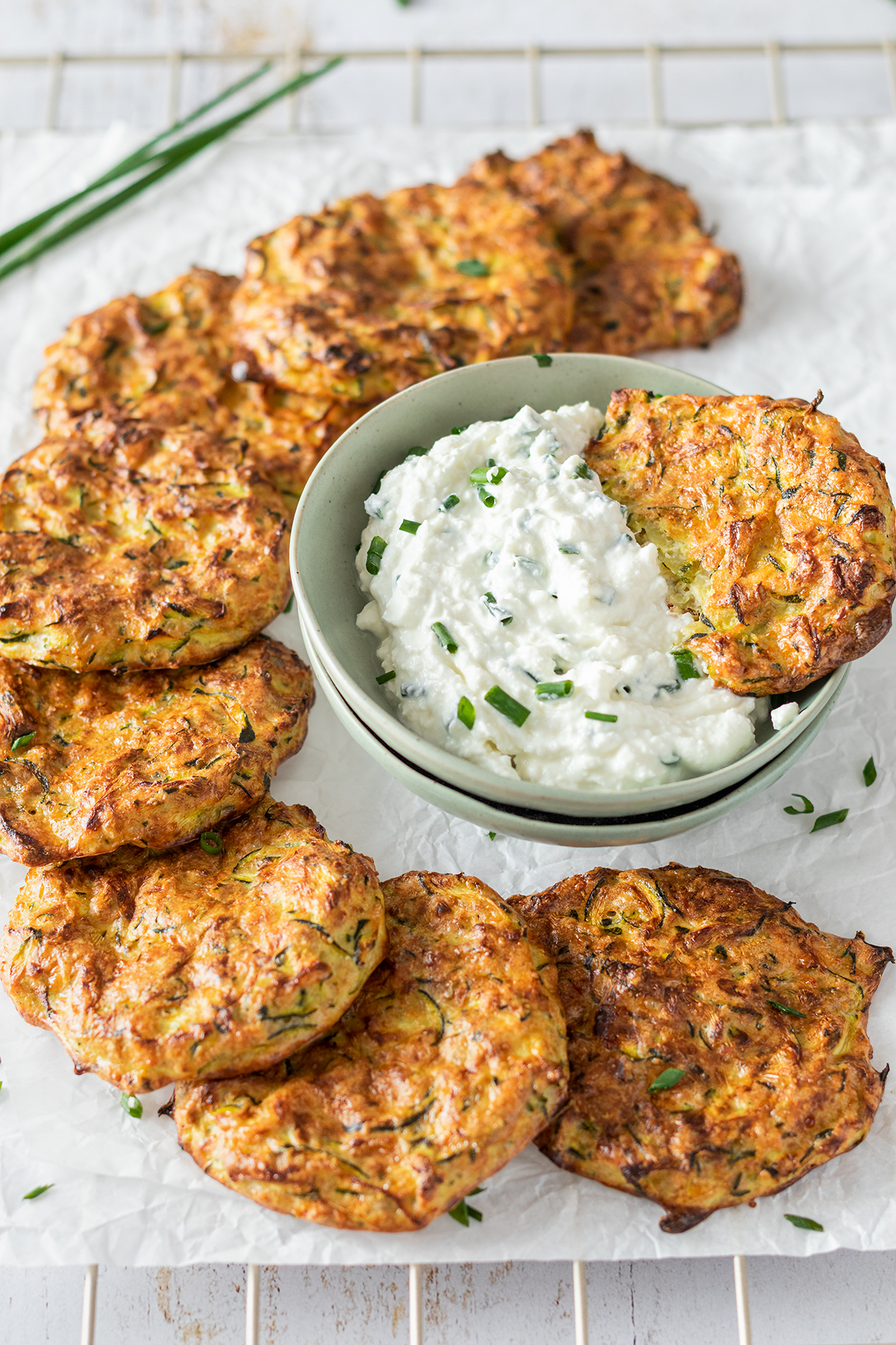 Knusprige Zucchinipuffer auf einem Ausk&uuml;hlgitter, serviert mit einem cremigen Dip.