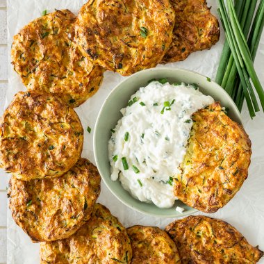 Knusprige Zucchinipuffer auf einem Ausk&uuml;hlgitter, serviert mit einem cremigen Dip.